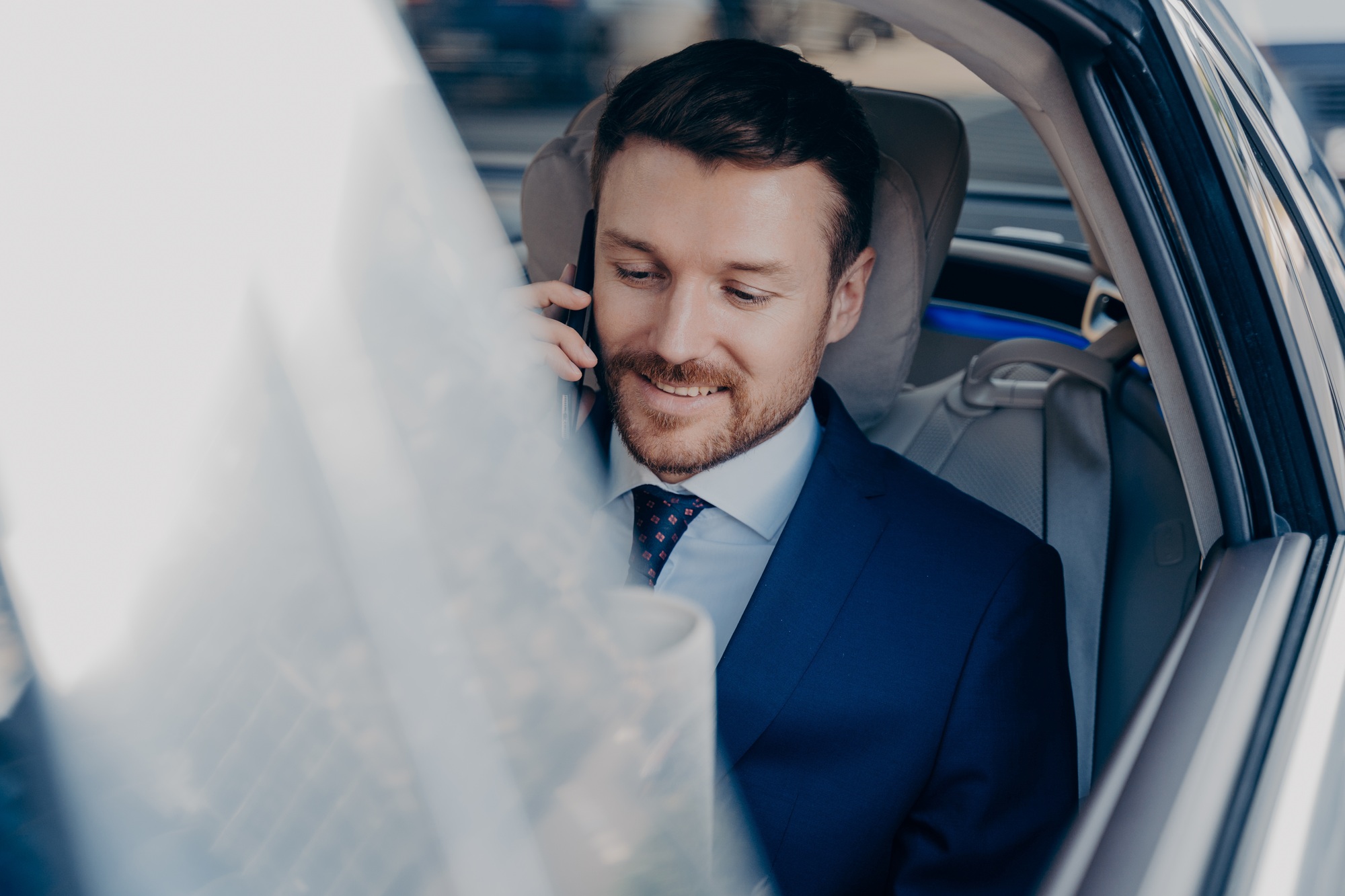 Businessman rides in black car in passenger seat and talking on cellphone