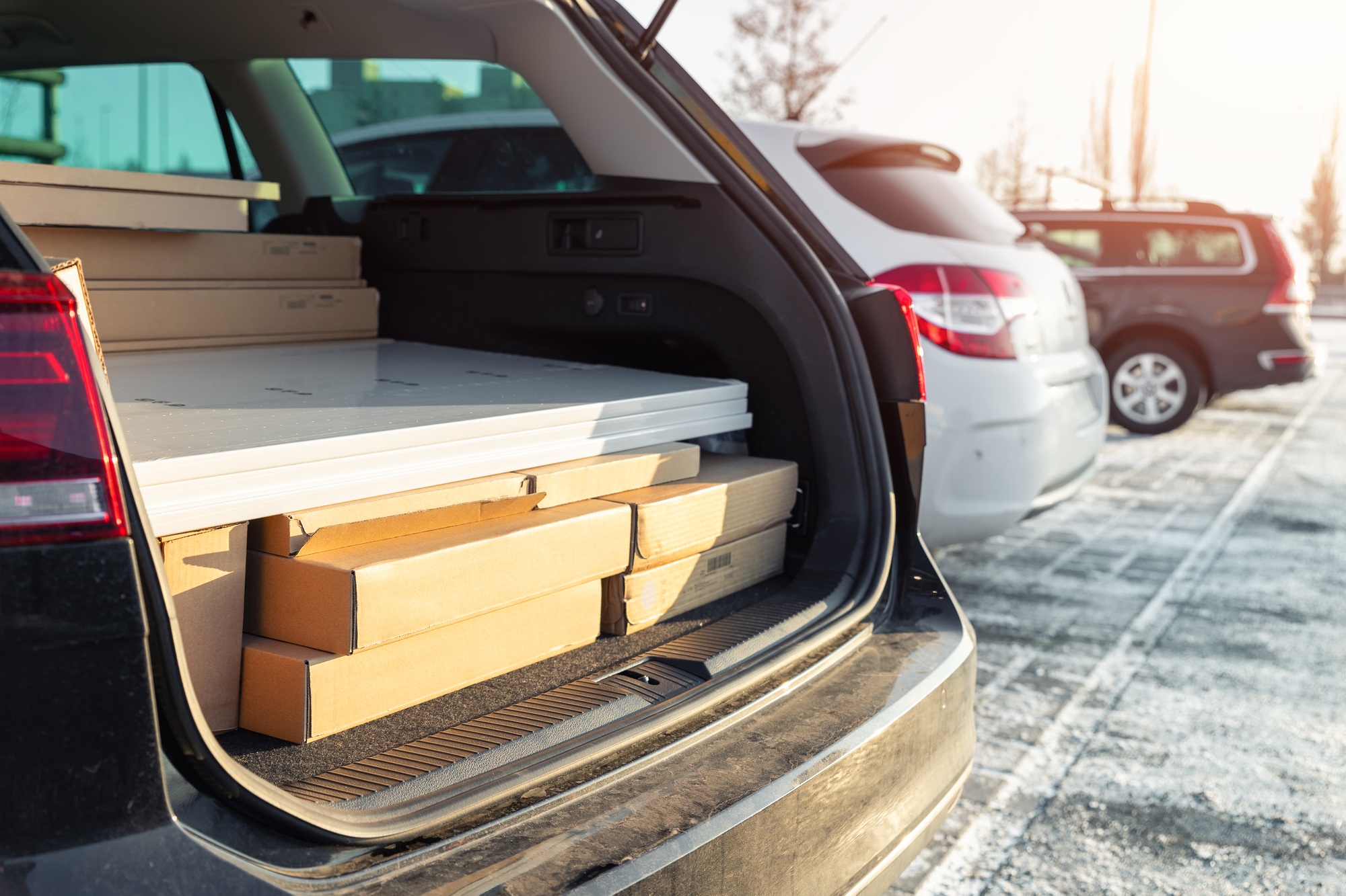 Modern black car wagon with open boot trunk back door fully loaded with furniture cardboard box